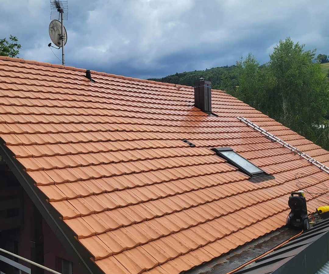 Toiture après lavage : tuiles rouges propres, avec la lance de nettoyage sur le toit